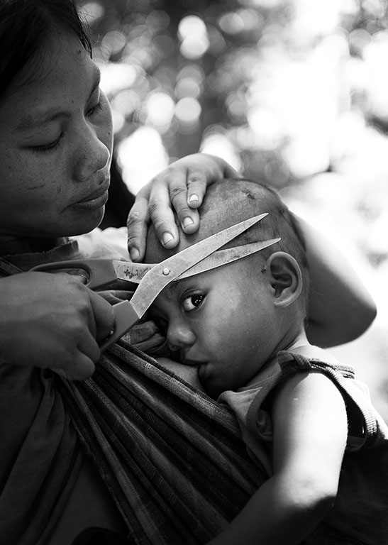 A mother gives her baby a haircut and feed at the same time. Luangprabang, Northern Laos Tour. 